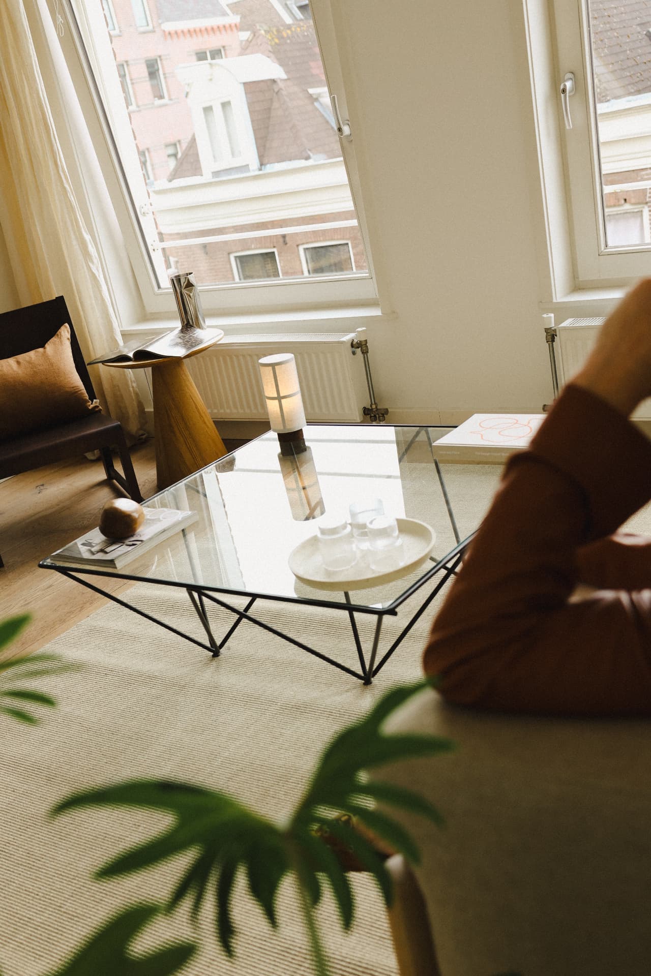 Woonkamer met glazen salontafel, tijdschriften en zacht daglicht door linnen gordijnen