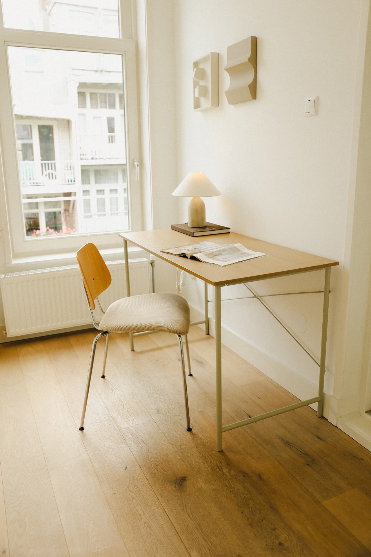 Werkplek met houten bureau, tafellamp en reliëfkunst aan de wand