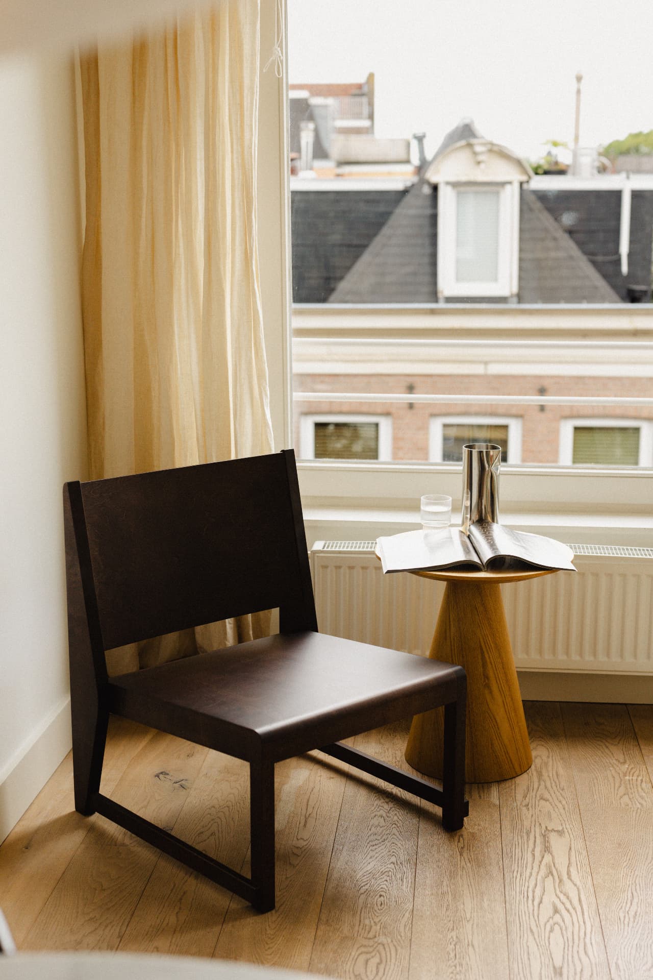 Donkere houten fauteuil naast een ronde bijzettafel bij het raam