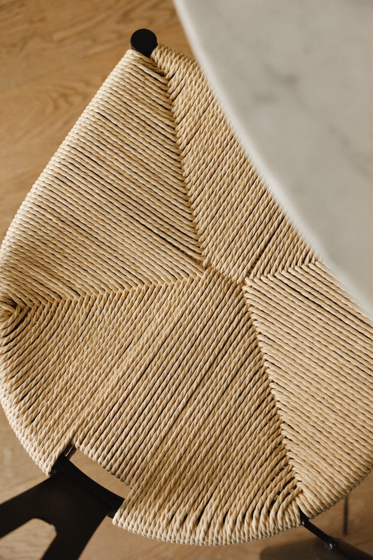 Detail van een gevlochten papercord stoelzitting bij een marmeren tafel